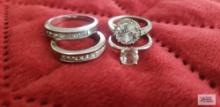 Four silver colored clear gemstone rings, one has marking of U with arrow through it